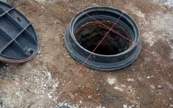 Żeliwny właz koloru czarnego posadowiony na studni kanalizacyjnej w celu regulacji wysokości tej studni