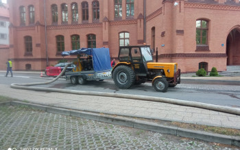 Na ulicy Sądowej w Braniewie obok Sądu Rejonowego w Braniewie żółty ciągnik rolniczy, który ma na przyczepce pompę przewoźną do przepompowania ścieków.  